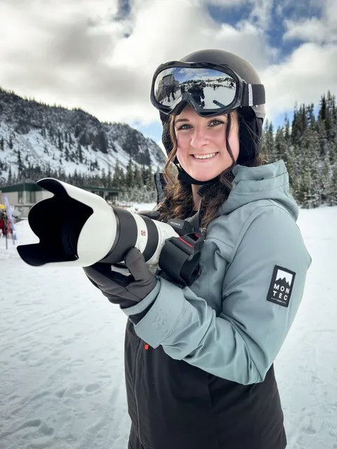 Marin on a snowy mountain in ski gear, holding a telephoto lens